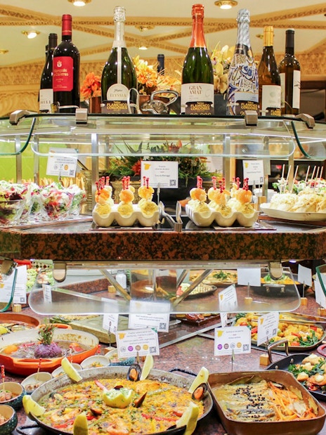 Food assortment at Tablao Cordobes buffet with paella, tapas, and wine bottles.