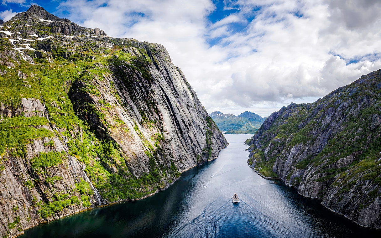 Aerial view of a boat cruising through Trollfjord, surrounded by steep cliffs in Lofoten.