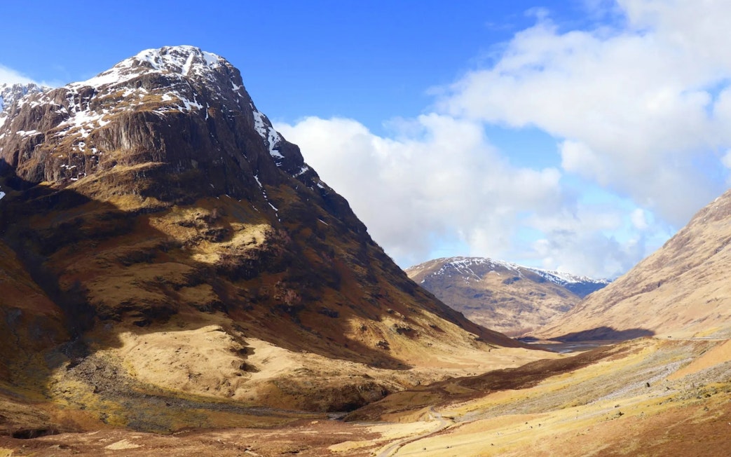 Glencoe valley with snow-capped mountains and a winding path under a blue sky.