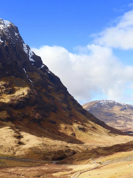 Glencoe valley with snow-capped mountains and a winding path under a blue sky.