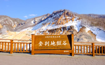 Noboribetsu Hell Valley sign with snow-covered volcanic landscape, Hokkaido.