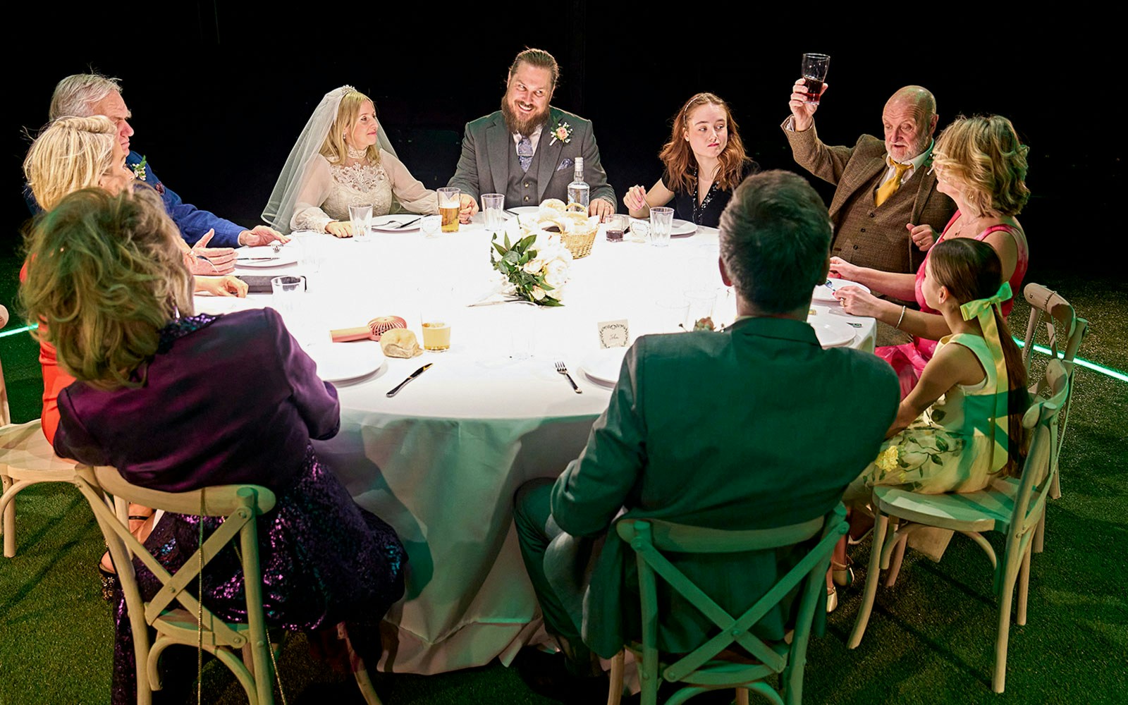 Wedding guests seated around a table, one raising a glass, during the "Till The Stars Come Down" event.