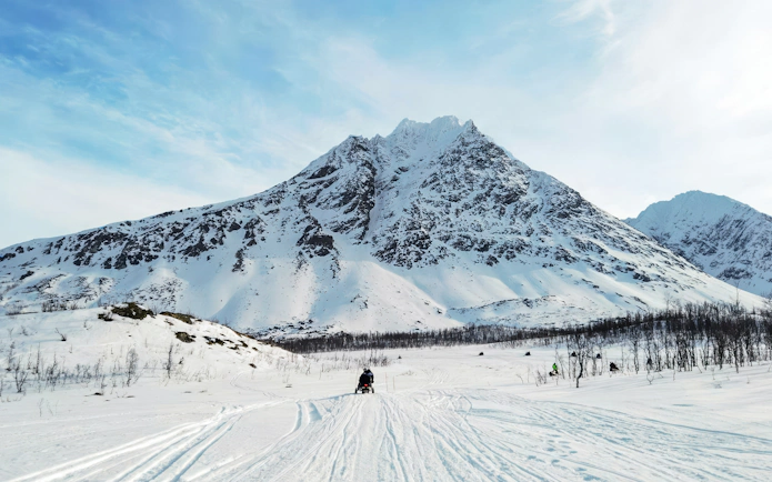Snowmobile rider in the Lyngen Alps, Tromsø, with snowy mountain backdrop.