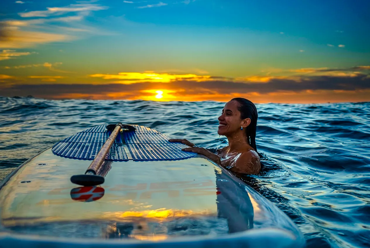 Woman enjoying stand-up paddleboarding at sunrise in Rio de Janeiro.