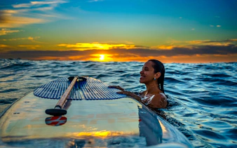 Woman enjoying stand-up paddleboarding at sunrise in Rio de Janeiro.