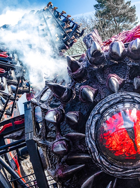 Roller coaster on Nemesis Reborn ride at Alton Towers with dramatic smoke effects.