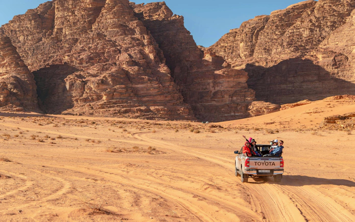 Tourists in a pickup truck exploring Wadi Rum desert landscape, Jordan.