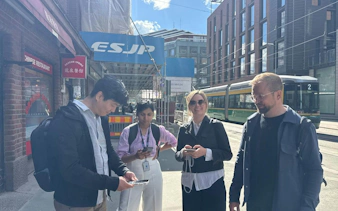 Participants engaging in Helsinki Murder Mystery game on a city street with tram in background.