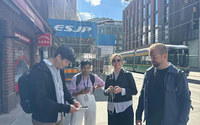 Participants engaging in Helsinki Murder Mystery game on a city street with tram in background.