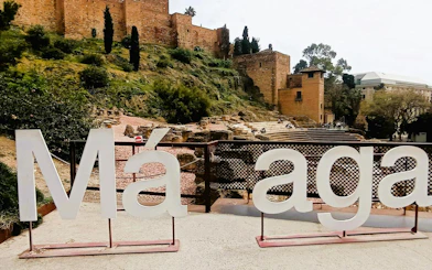 Malaga city sign with Alcazaba fortress in the background, part of self-guided exploration game.