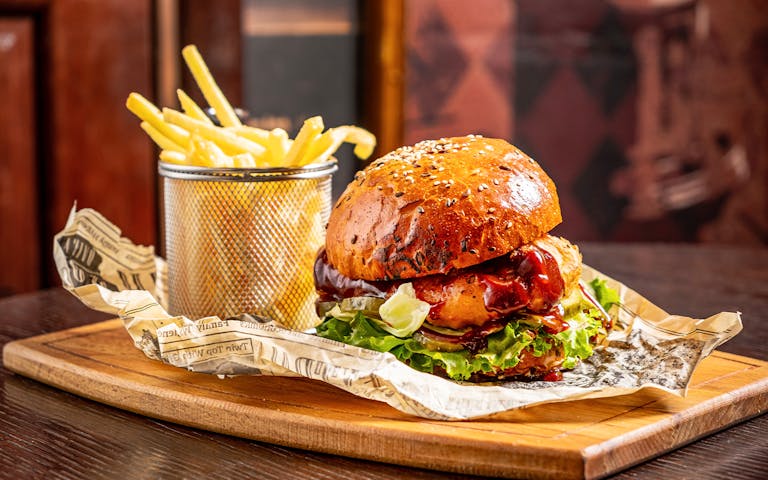 Burger with lettuce and sauce on a wooden board, served with fries in a metal cup.