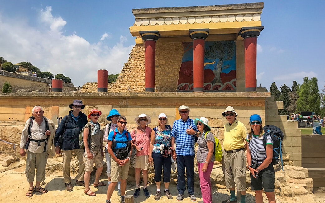 Group of tourists at Knossos Palace, Crete, with ancient ruins and fresco in the background.