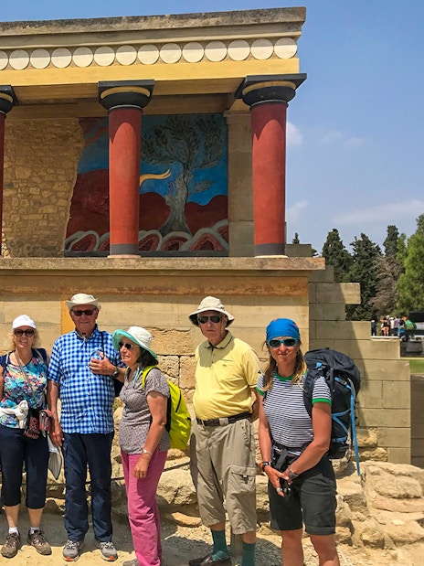 Group of tourists at Knossos Palace, Crete, with ancient ruins and fresco in the background.