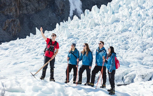 Guide explaining glacier hiking techniques to group on ice.