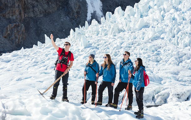 Guide explaining glacier hiking techniques to group on ice.