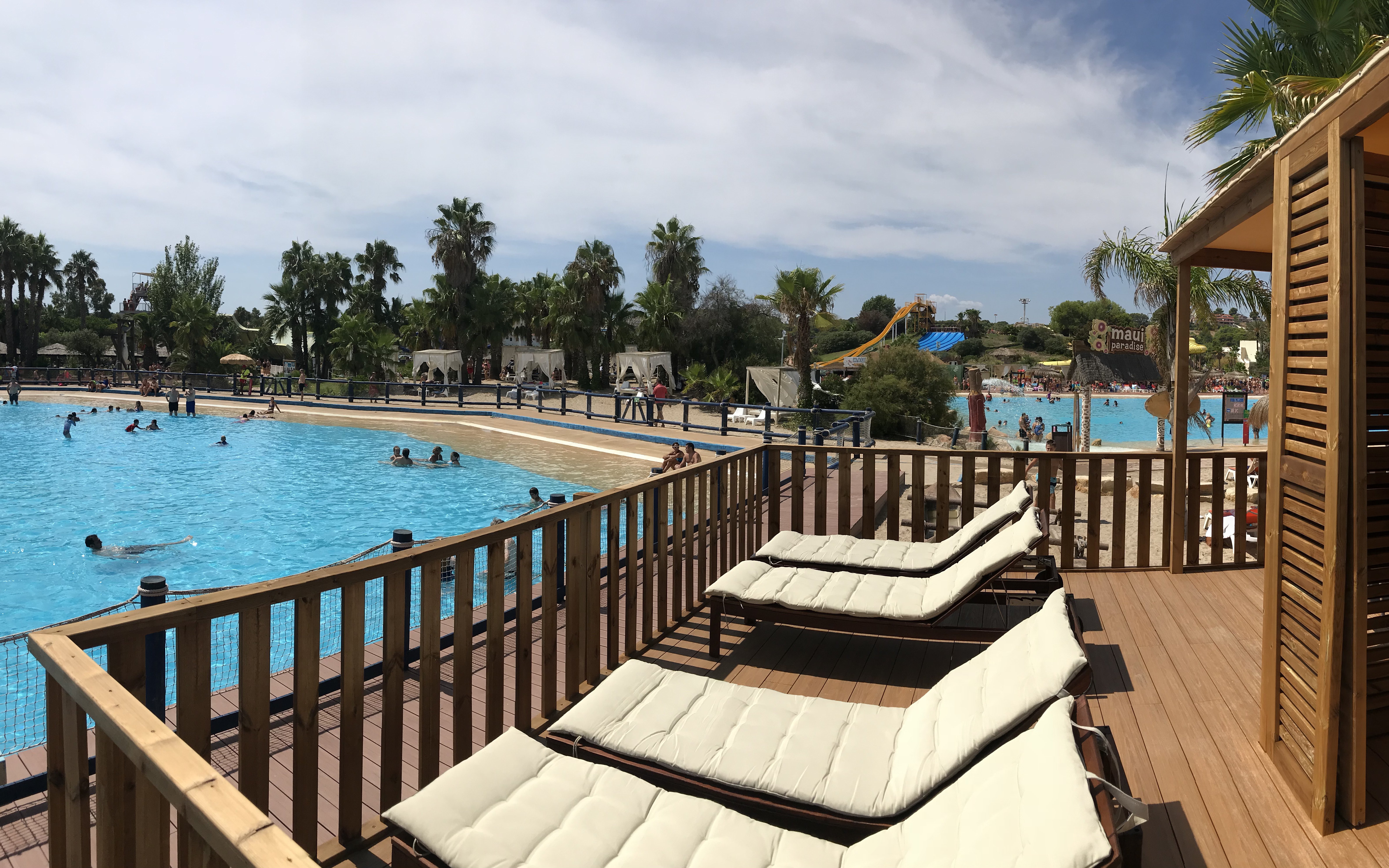 Sun loungers by the pool at Aquopolis Costa Daurada, Tarragona water park with slides and palm trees.