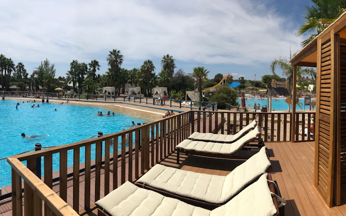 Sun loungers by the pool at Aquopolis Costa Daurada, Tarragona water park with slides and palm trees.
