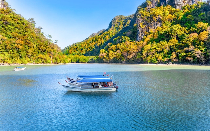 Boat on the water with lush hills in Kilim Geoforest Park, Langkawi, Malaysia.