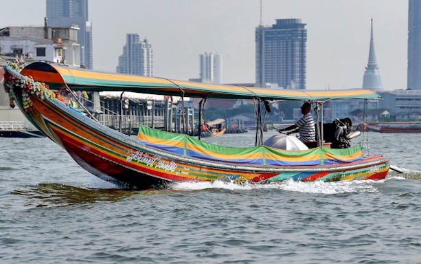Long-tail boat navigating Bangkok Yai Canal with city skyline in background.