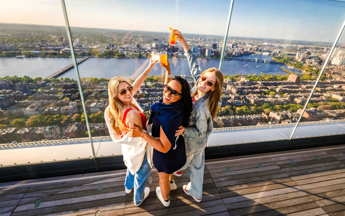Group enjoying drinks with a panoramic view of Boston skyline from an observation deck.