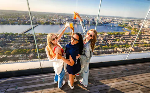 Group enjoying drinks with a panoramic view of Boston skyline from an observation deck.