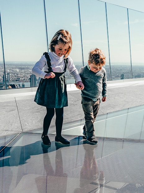 Children walking on glass floor at Edge Observation Deck, New York City skyline in background.