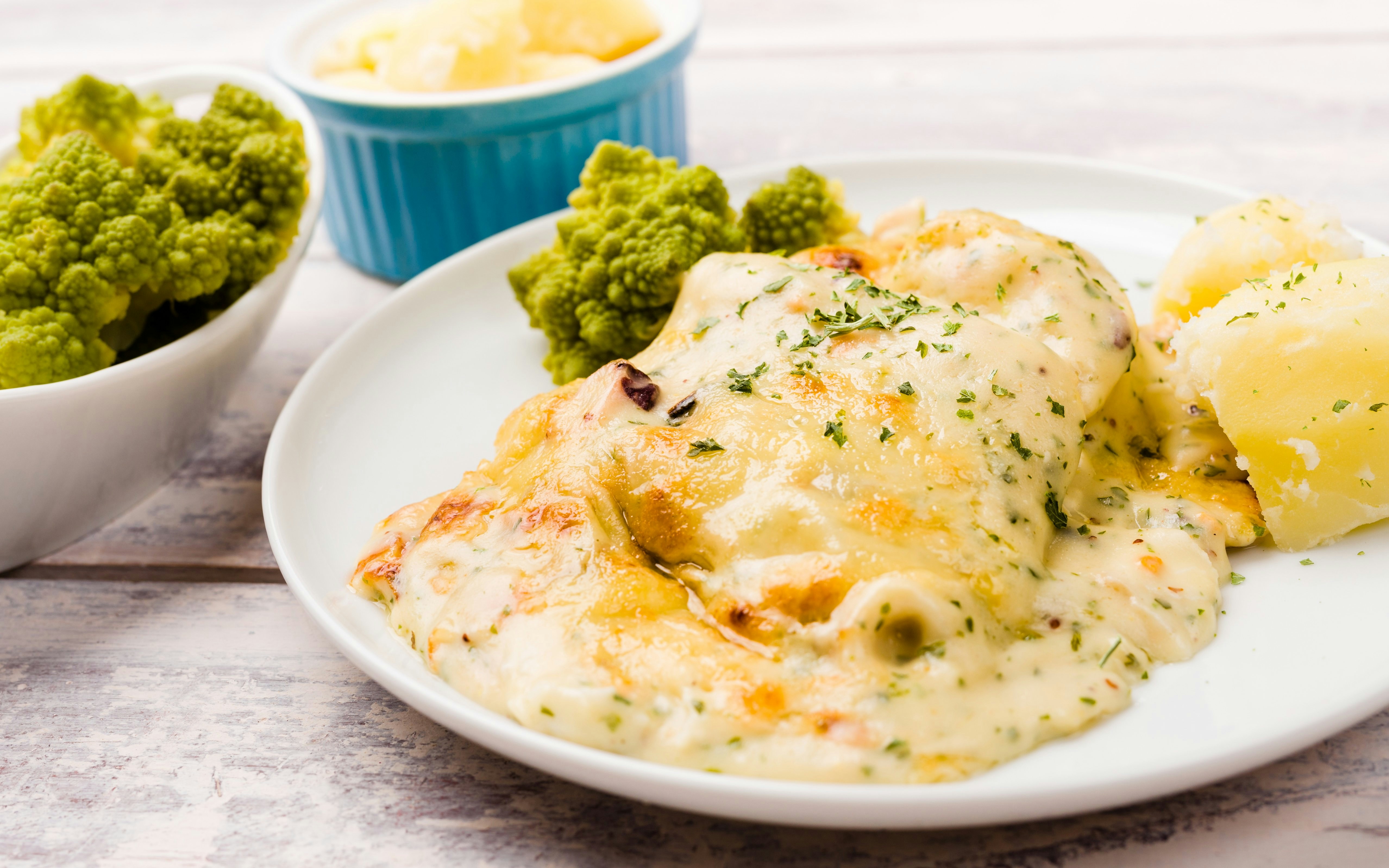 Cod fish casserole with cheese and seafood on a white plate, served with potatoes and romanesco cauliflower.