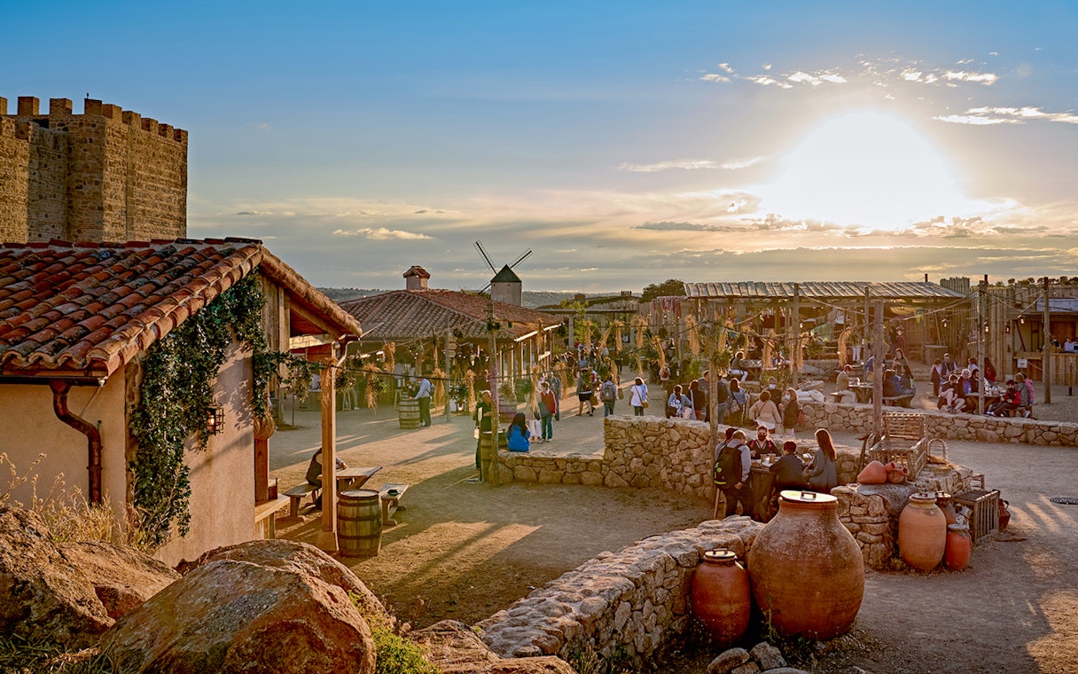 Puy du Fou España park village scene with visitors and sunset.