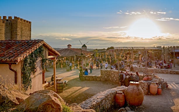 Puy du Fou España park village scene with visitors and sunset.