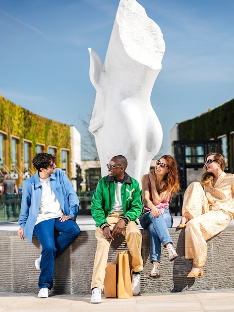 Friends sitting by a sculpture at McArthurGlen shopping center during Monet's House & Gardens tour.
