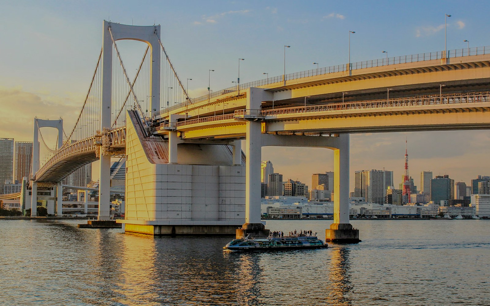 Rainbow Bridge in Tokyo, Japan during golden hour with city skyline in background.