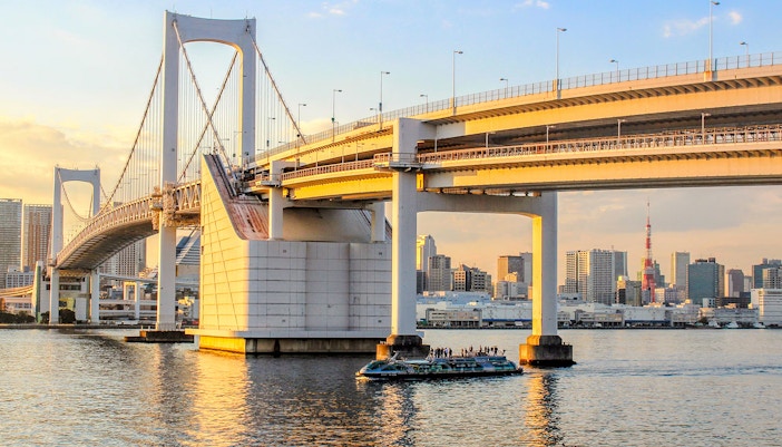 Rainbow Bridge in Tokyo, Japan during golden hour with city skyline in background.