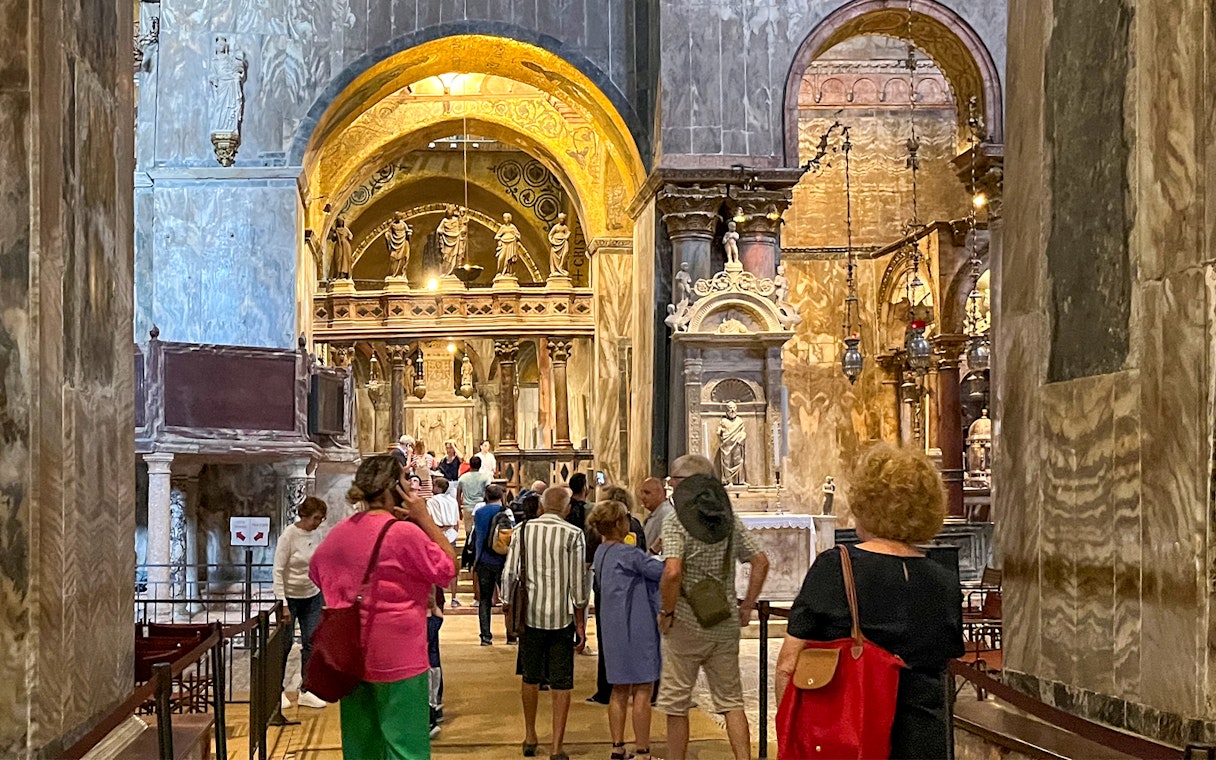 Visitors exploring the interior of St. Mark's Basilica, Venice, with ornate arches and statues.
