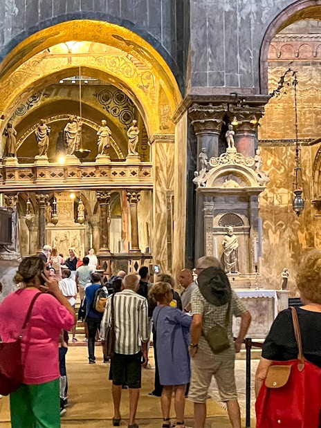 Visitors exploring the interior of St. Mark's Basilica, Venice, with ornate arches and statues.