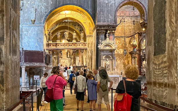 Visitors exploring the interior of St. Mark's Basilica, Venice, with ornate arches and statues.