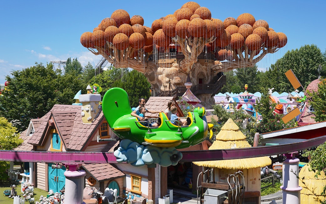 Visitors enjoying a ride at Gardaland Park with whimsical treehouse in background.