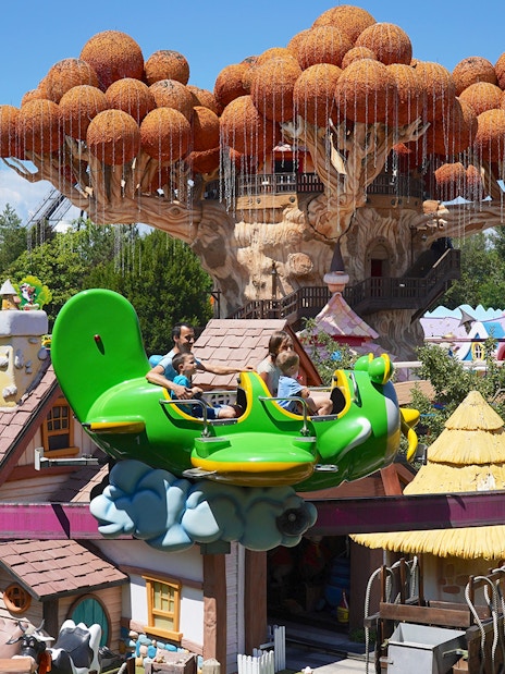 Visitors enjoying a ride at Gardaland Park with whimsical treehouse in background.