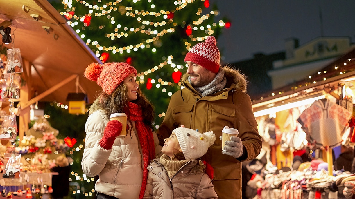 Family enjoying hot drinks at a festive Christmas market in the evening.