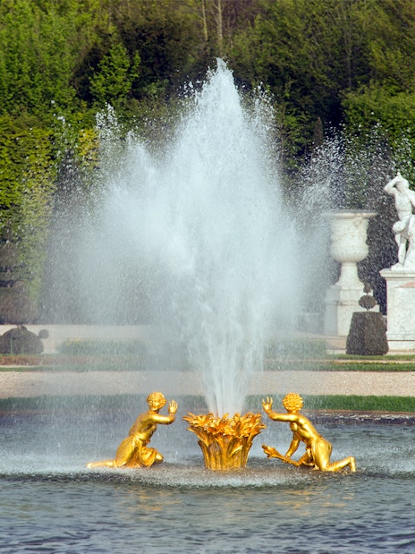 Fountain with golden statues at Palace of Versailles gardens, France.