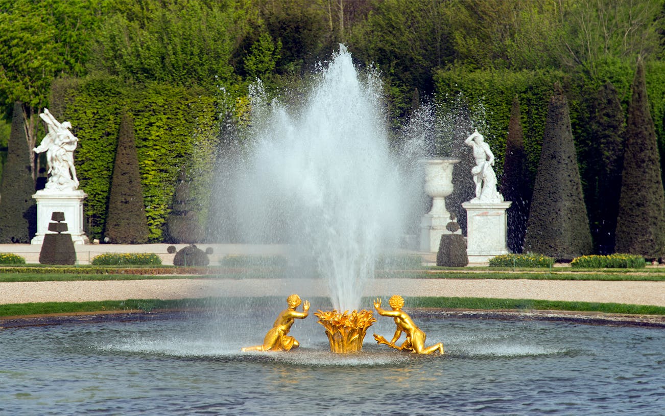 Fountain with golden statues at Palace of Versailles gardens, France.