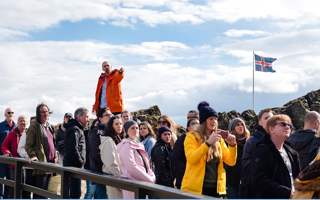 Tour group with guide at Thingvellir National Park, Icelandic flag in background.