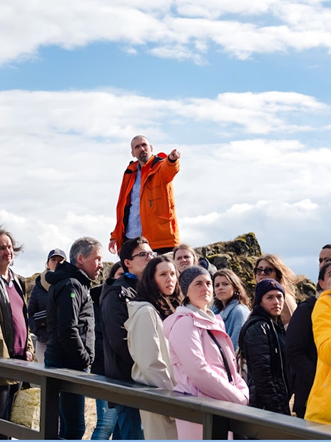 Tour group with guide at Thingvellir National Park, Icelandic flag in background.