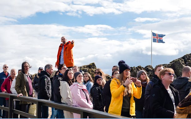 Tour group with guide at Thingvellir National Park, Icelandic flag in background.