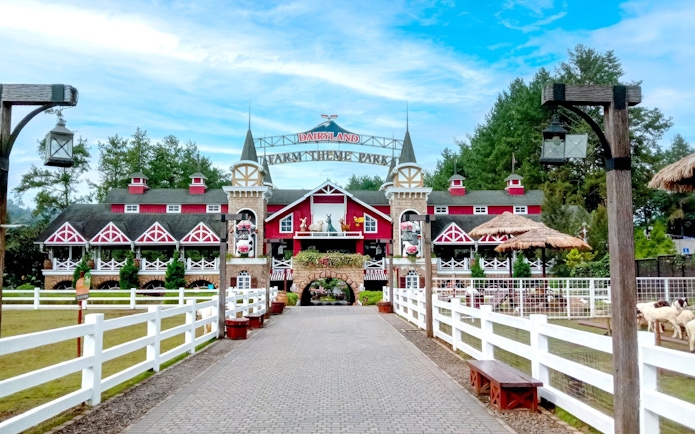 Entrance to Dairyland Farm Theme Park in Puncak with red barn-style building and white fences.