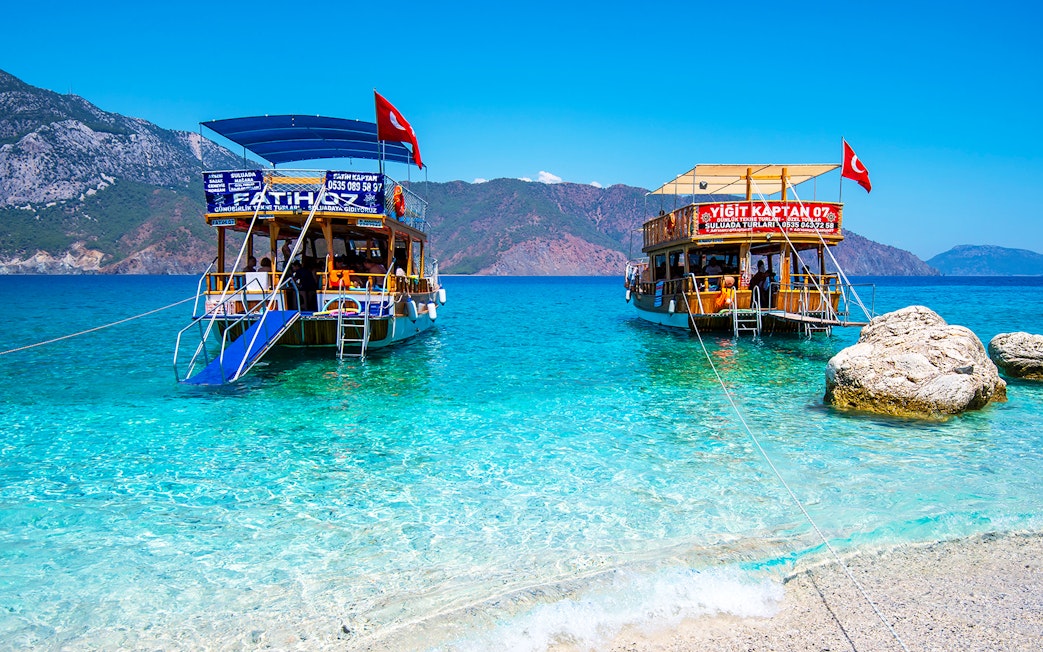 Boats anchored near Suluada Island, Antalya, with clear turquoise water and rocky shore.