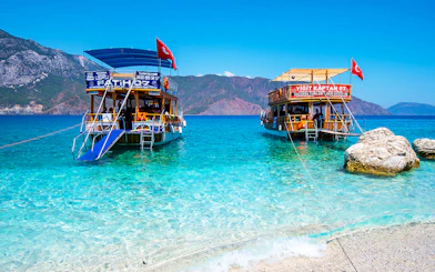 Boats anchored near Suluada Island, Antalya, with clear turquoise water and rocky shore.