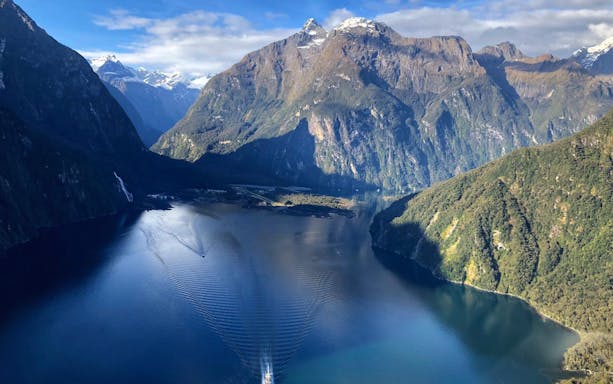 Aerial view of a tour boat cruising through Milford Sound's fiord and mountains in Queenstown.