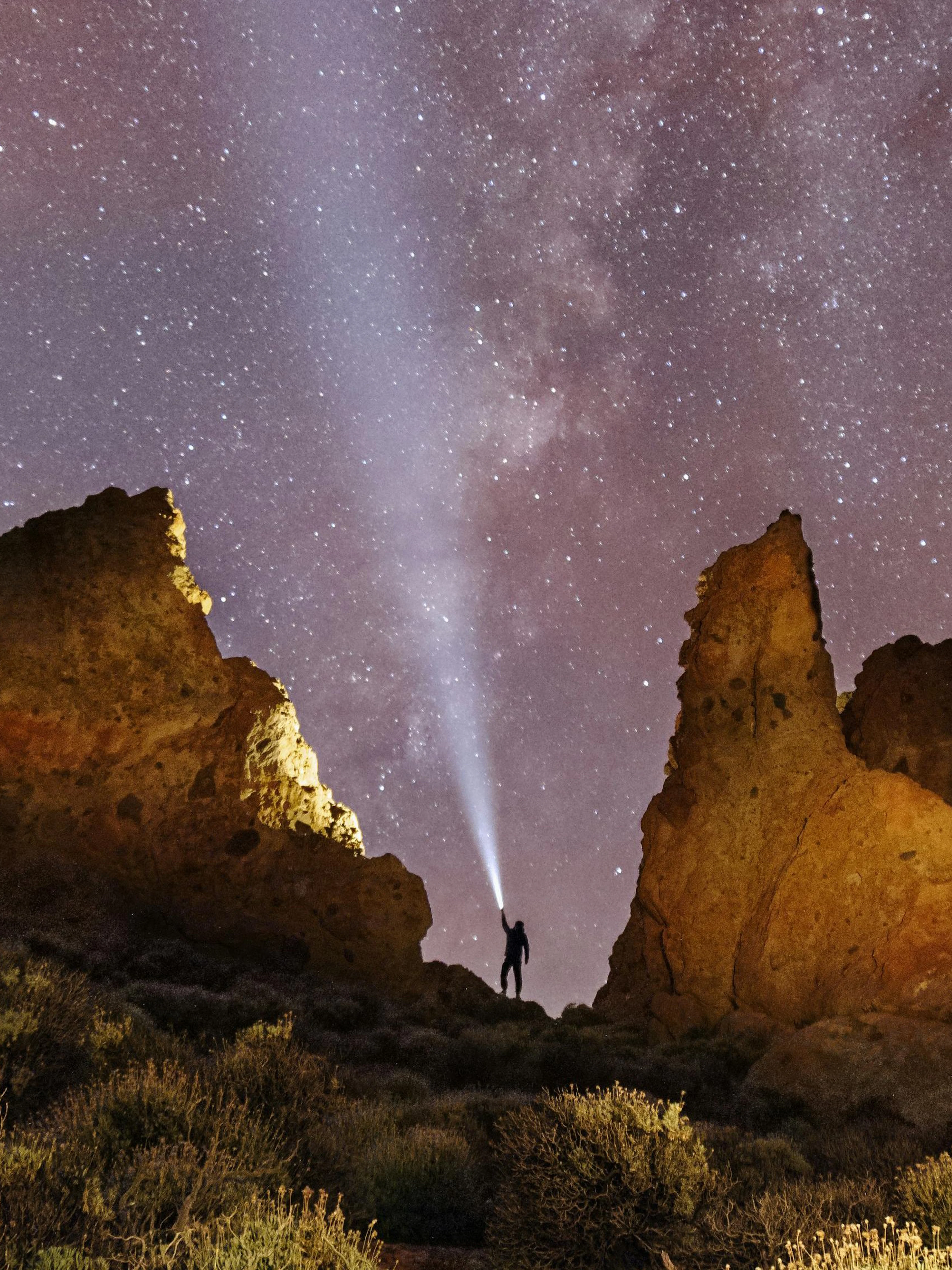 Person with flashlight near rock formations under Milky Way sky.