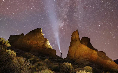 Person with flashlight near rock formations under Milky Way sky.
