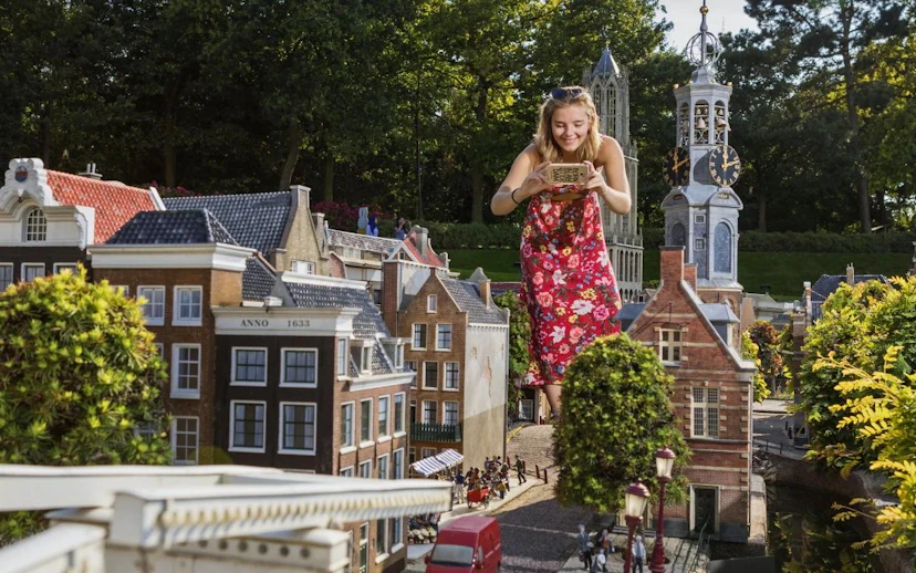 Woman photographing miniature Dutch buildings at Madurodam park.